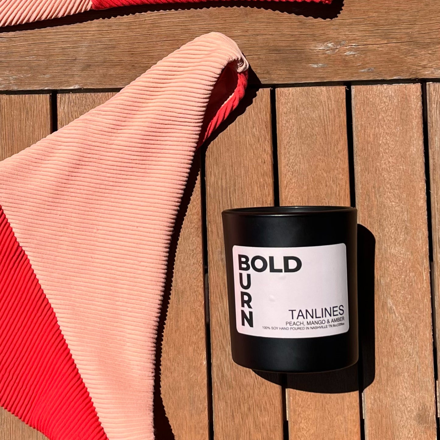Bold Burn two-wick candle Tanlines resting on a beach chair next to a colorful beach towel
