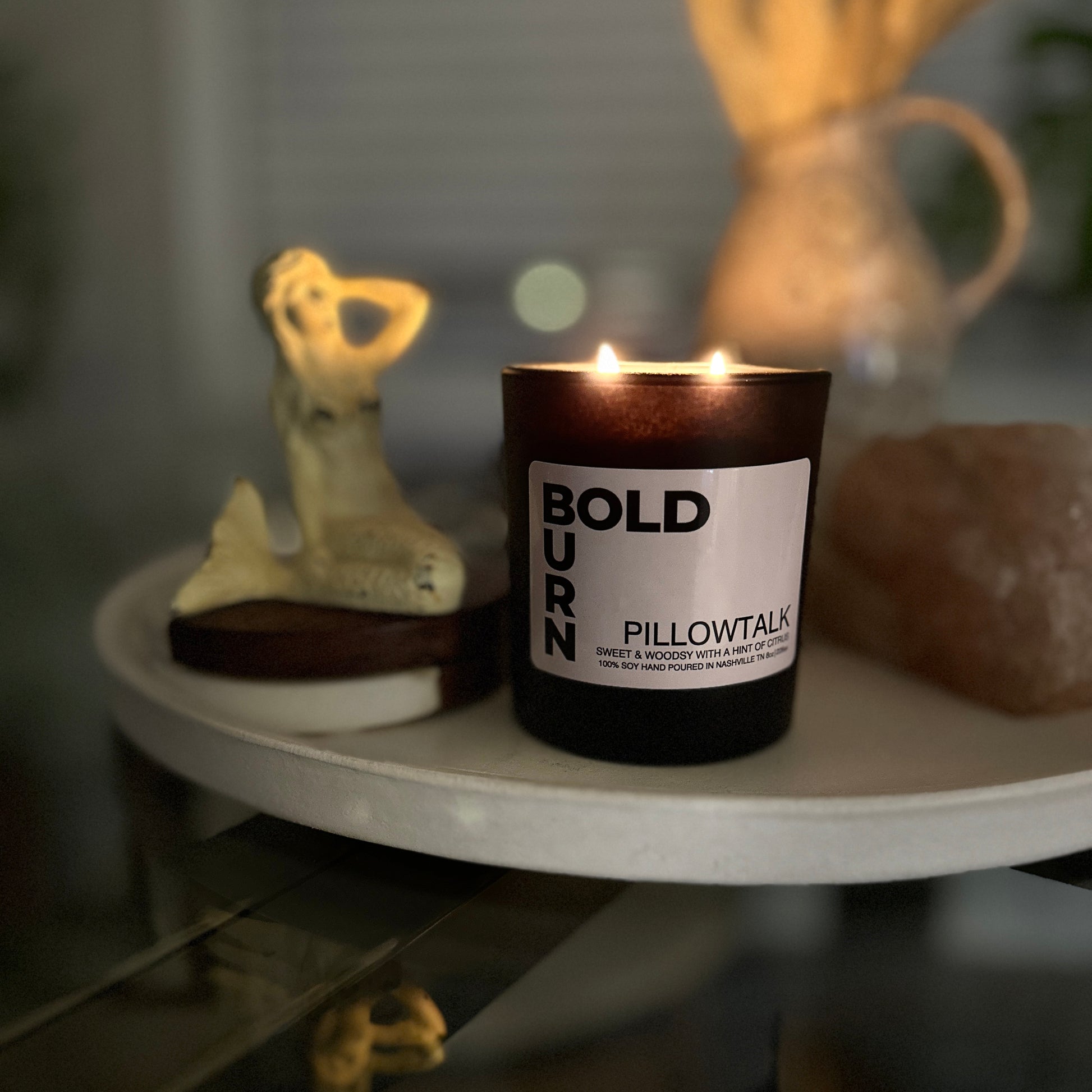 Bold Burn two-wick candle Pillowtalk on a round table with a figurine and rock
