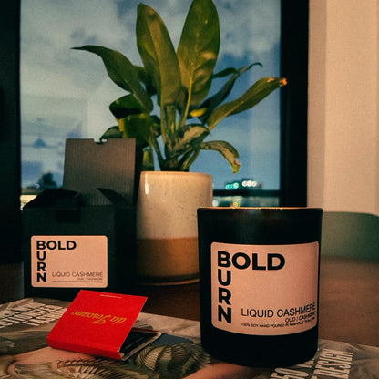 BoldBurn Liquid Cashmere two wick candle on a table with matches, candle gift box and plant